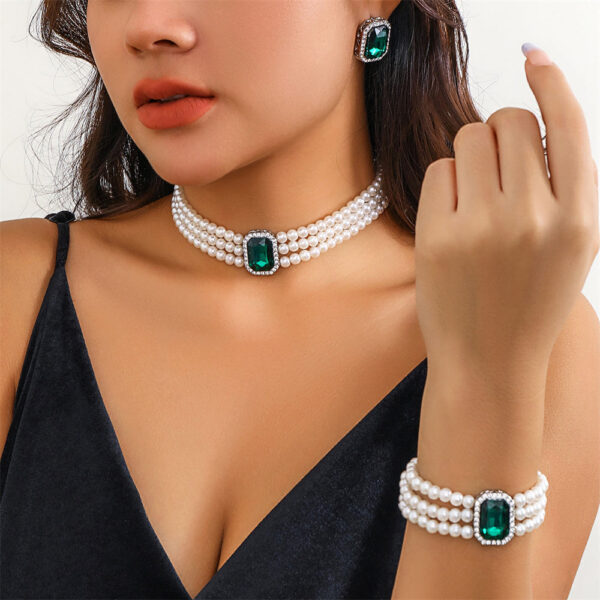 Large green emerald stones adorn this multilayer pearl jewellery set by Eclat New York, which includes a pearl bracelet, matching earrings, and a choker.