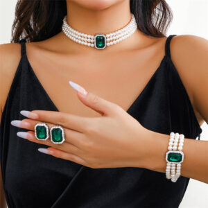 Large green emerald stones adorn this multilayer pearl jewellery set by Eclat New York, which includes a pearl bracelet, matching earrings, and a choker.